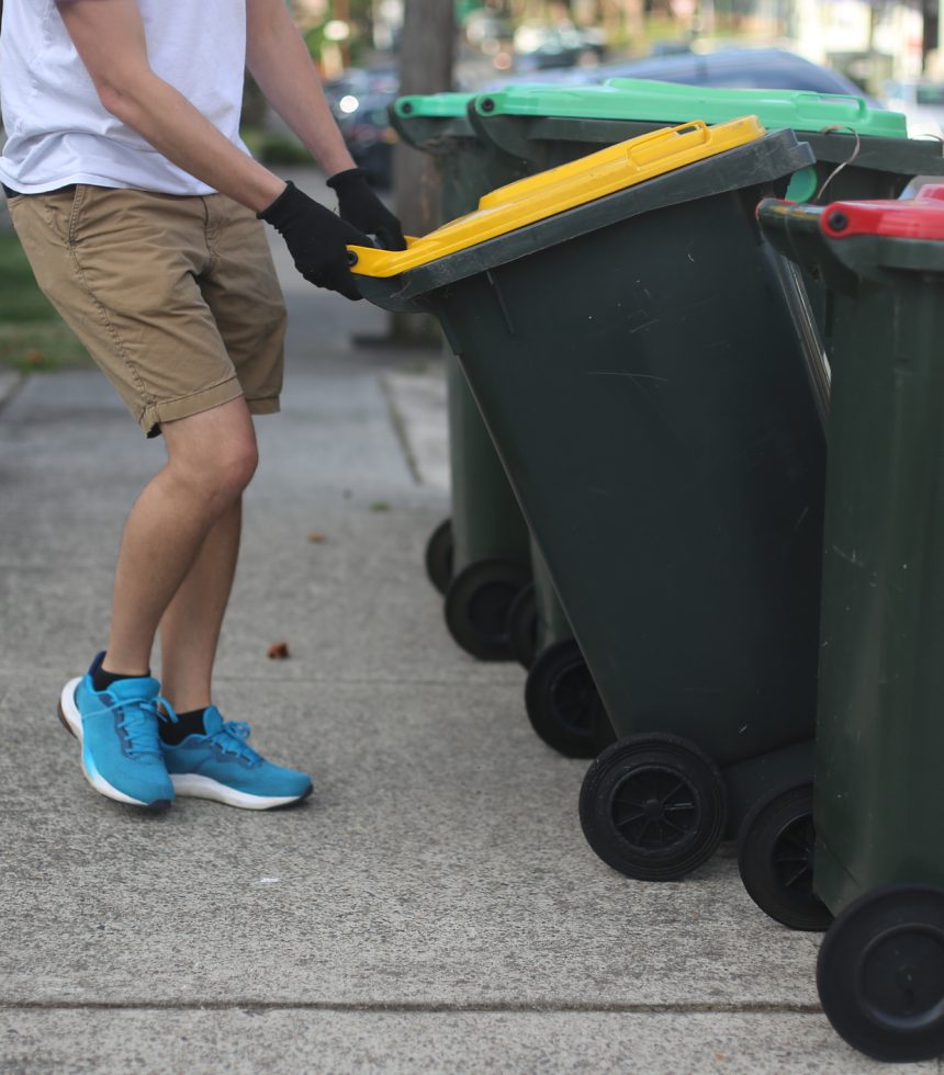 A person putting rubbish and recycling bins out for collection by a curb.